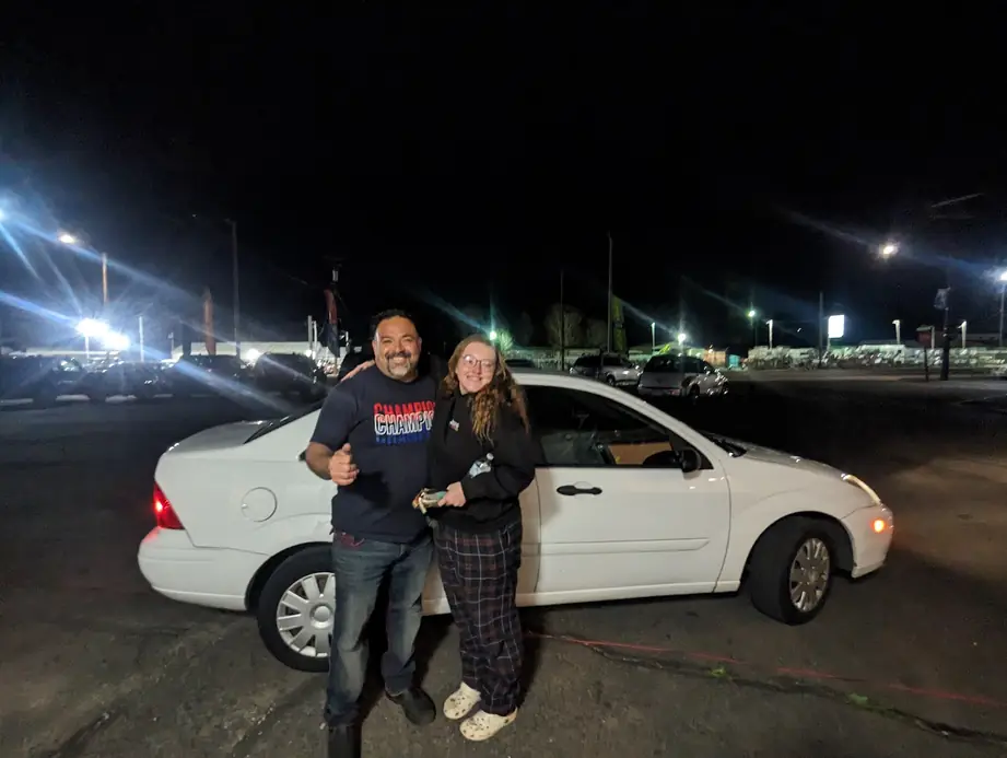 Juan Palomo with a customer and her white Ford Focus on the lot at night